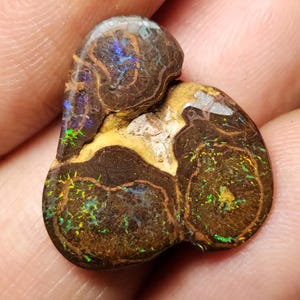 May include: A brown, green, and blue opal with a swirling pattern. The opal is a natural gemstone with a unique and beautiful appearance.