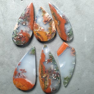 Puede incluir: Seis cabujones de ágata en forma de lágrima con una mezcla de colores blanco, marrón, rojo y verde. Las piedras están pulidas y tienen un acabado liso y brillante.