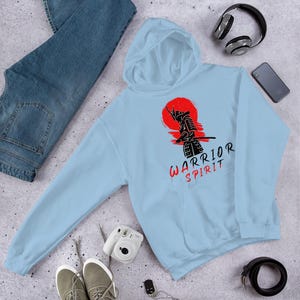 May include: Light blue hoodie with a black silhouette of a samurai warrior in front of a red sun. The text "WARRIOR SPIRIT" is printed below the image.