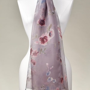 Könnte beinhalten: Ein transparenter, rechteckiger Schal in einem gedeckten Mauveton mit einem zarten Blumenmuster aus aquarellartigen Blüten in Dunkelrot, zartem Rosa und Hellblau, der elegant um einen weißen Schaufensterpuppenhals drapiert ist.