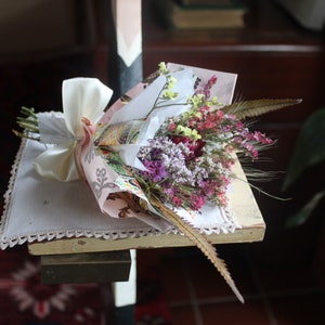 The pink bouquet with ferns wrapped with pink and gold wrapping paper lying flat on a display piece.