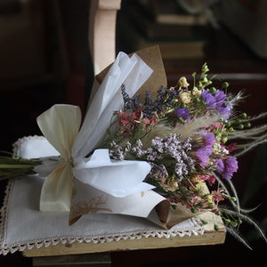 The purple bouquet with feathery grasses wrapped with pink and gold wrapping paper lying flat on a display piece.