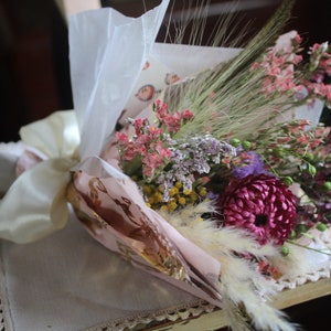 The pink and purple bouquet wrapped with pink and gold wrapping paper lying flat on a display piece.