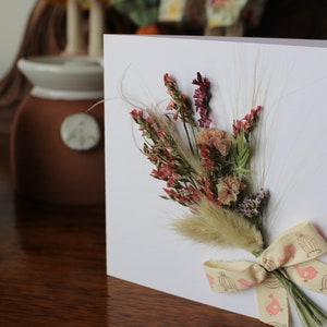 A mini bouquet of pinks, peaches and bunnies tails with a cream and pink ribbon on a gift card.
