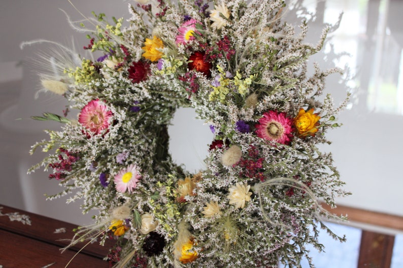 The wreath is proped up against a pain of glass and sitting on a wooden table.