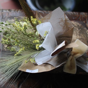 The yellow bouquet with grasses wrapped with gold and white wrapping paper lying flat on a display piece.