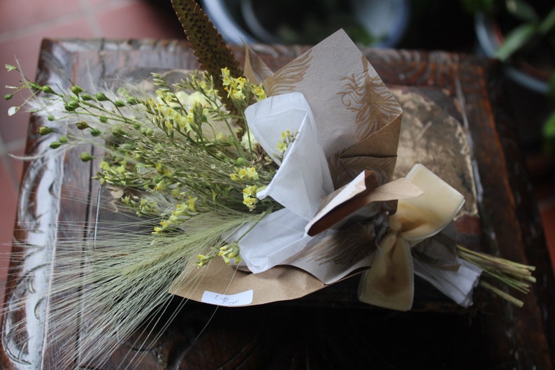 The yellow bouquet with grasses wrapped with gold and white wrapping paper lying flat on a display piece.