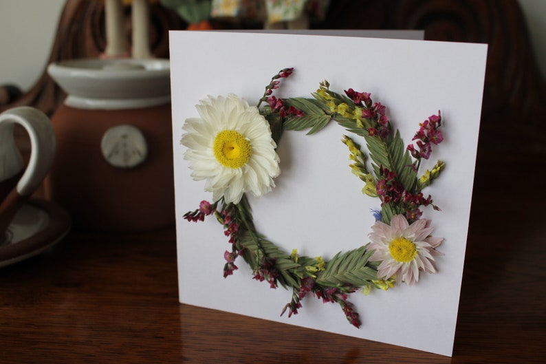 A mini wreath of grasses, statice and daisy like flowers on a gift card.