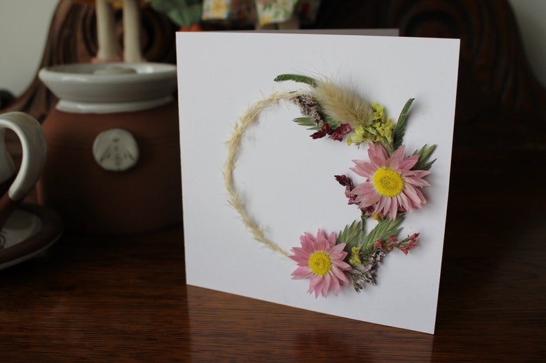 A mini wreath of grasses, statice and pink daisy like flowers on a gift card.