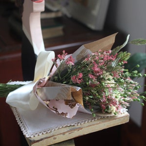 The purple and green mini bouquet wrapped in pink and gold wrapping paper.