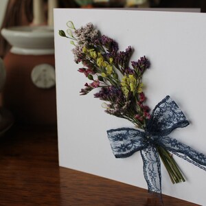 A mini bouquet of purple and yellow statice with a blue lace on a gift card.