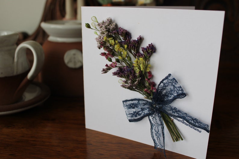 A mini bouquet of purple and yellow statice with a blue lace on a gift card.