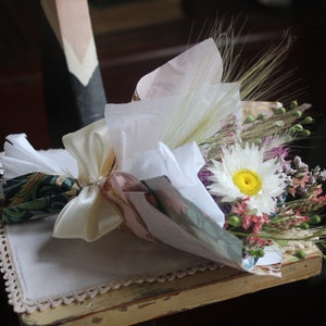 The daisy  bouquet wrapped with white and gold wrapping paper lying flat on a display piece.