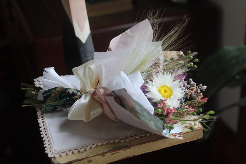 The daisy  bouquet wrapped with white and gold wrapping paper lying flat on a display piece.