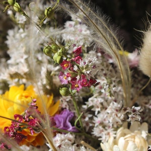 An up close image of the flowers in the wreath. The grasses and seed pods can be seen clearly and the  white and golden yellow straw flowers.