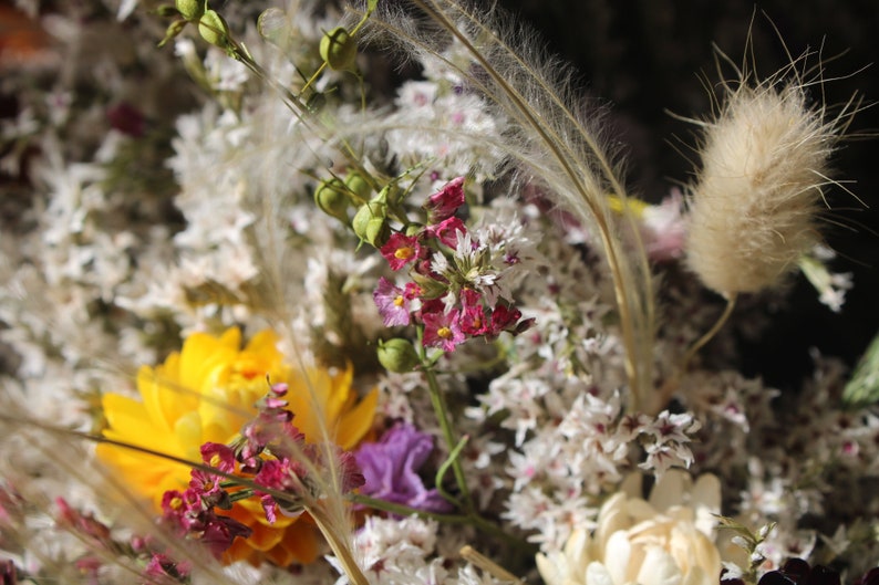 An up close image of the flowers in the wreath. The grasses and seed pods can be seen clearly and the  white and golden yellow straw flowers.