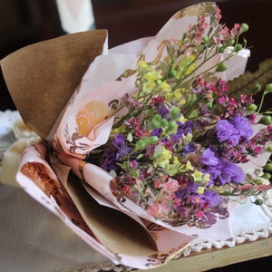 The purple and yellow bouquet wrapped with pink and gold wrapping paper lying flat on a display piece.