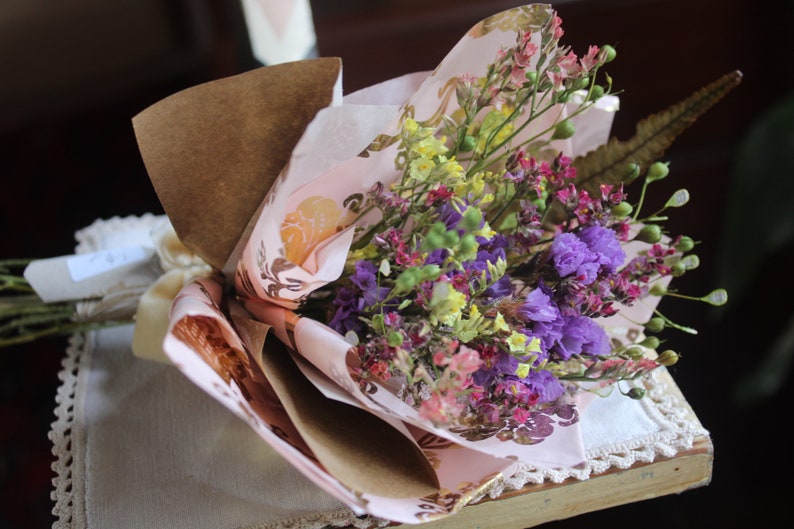 The purple and yellow bouquet wrapped with pink and gold wrapping paper lying flat on a display piece.