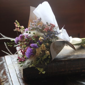 The purple bouquet wrapped with gold and white wrapping paper lying flat on a book on a dark wooden stool.