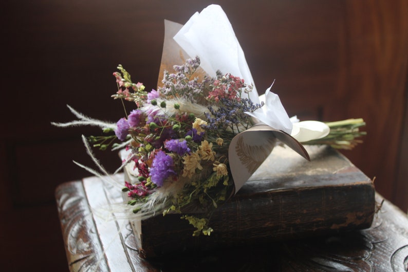 The purple bouquet wrapped with gold and white wrapping paper lying flat on a book on a dark wooden stool.