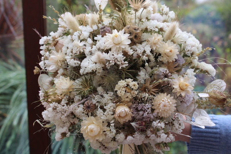 The white bouquet being held in a hand. The details of the flowers shape are more obvious in this photo.
