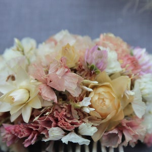 The pink pastel and peach small hair comb up close. The star like structure of the white and cream straw flower sits beside the delicate folds of the peach and pastel pink staice flowers in which nestles the small spires of the pink gomphrena.