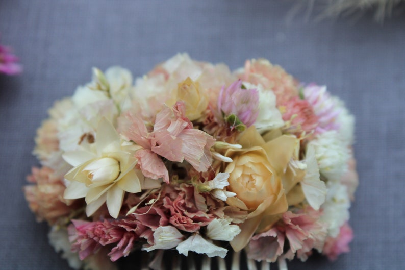 The pink pastel and peach small hair comb up close. The star like structure of the white and cream straw flower sits beside the delicate folds of the peach and pastel pink staice flowers in which nestles the small spires of the pink gomphrena.