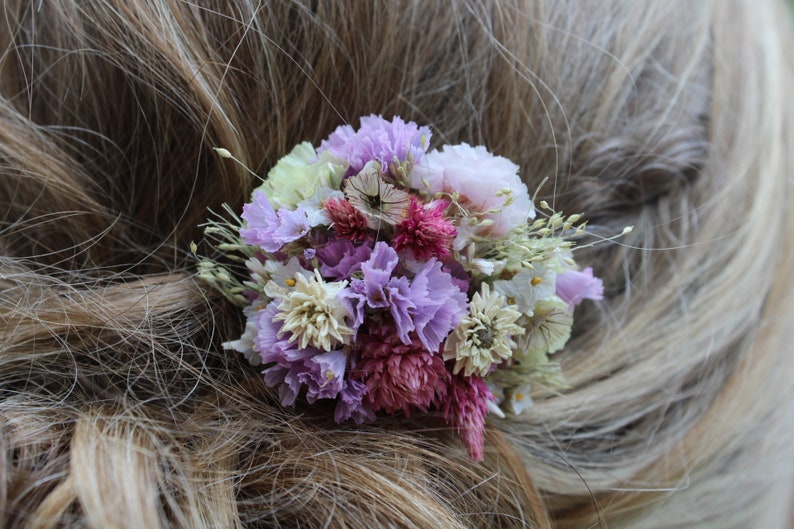 A closer photo of the small purple comb in an up do hair style. The comb is positioned on the side of the hair. The hair model has light brown hair with blonde highlights