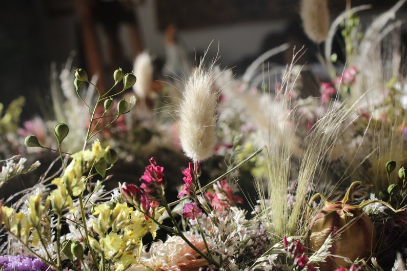 An up close image of the flowers in the wreath. The grasses and seed pods can be seen clearly and the purple and yellow flowers.