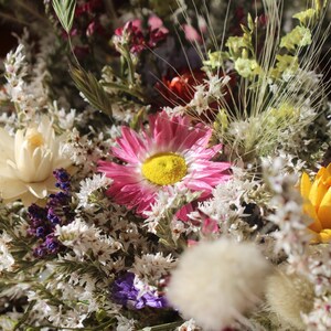 An up close image of the flowers in the wreath. The grasses and seed pods can be seen clearly and the pink, white and yellow flowers.