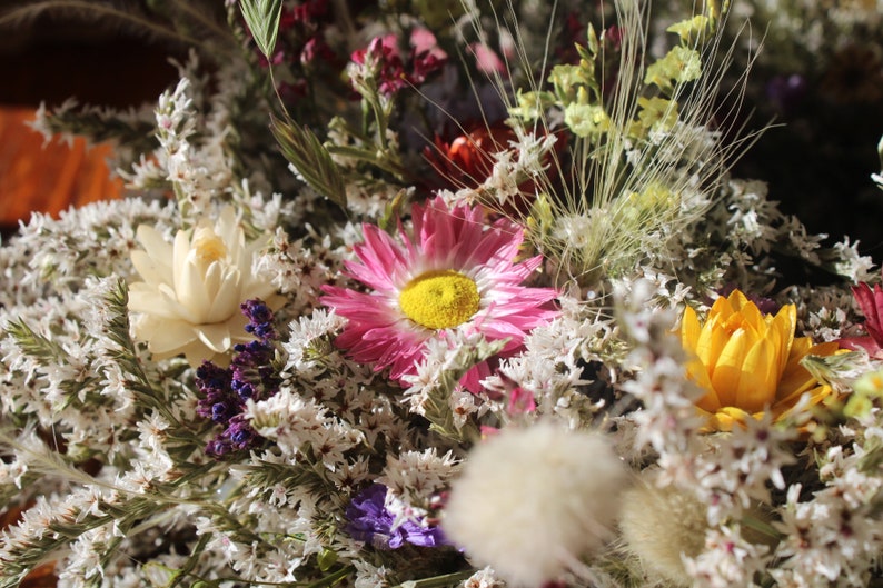 An up close image of the flowers in the wreath. The grasses and seed pods can be seen clearly and the pink, white and yellow flowers.