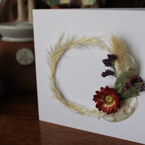 A mini wreath of grasses, straw flower and statice on a gift card.