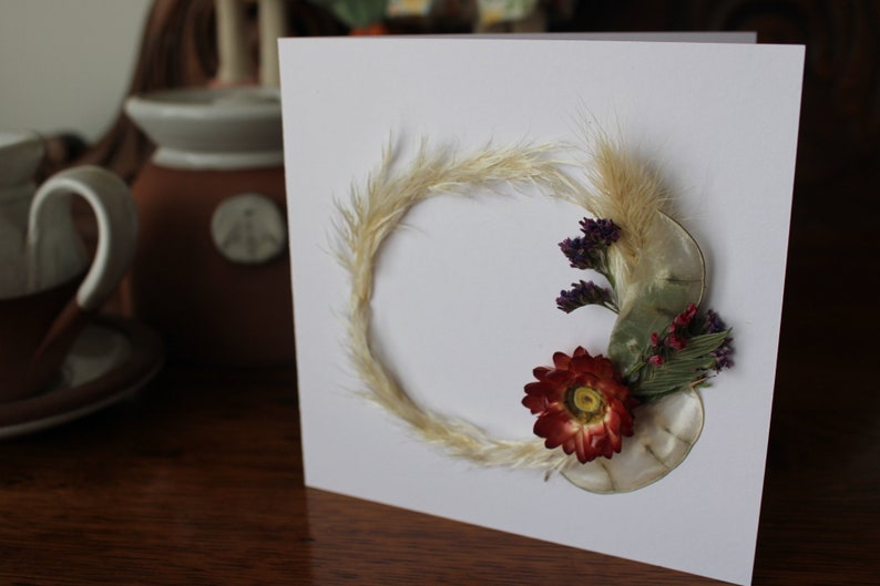A mini wreath of grasses, straw flower and statice on a gift card.