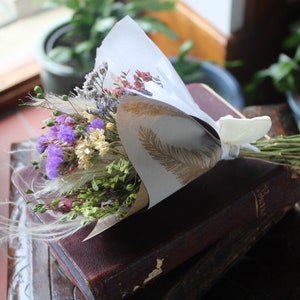 The purple bouquet wrapped with gold and white wrapping paper lying flat on a book on a dark wooden stool.