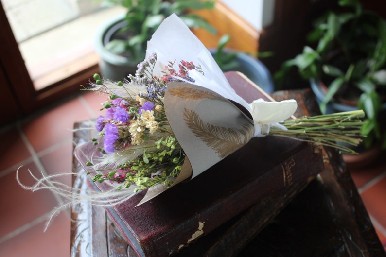 The purple bouquet wrapped with gold and white wrapping paper lying flat on a book on a dark wooden stool.