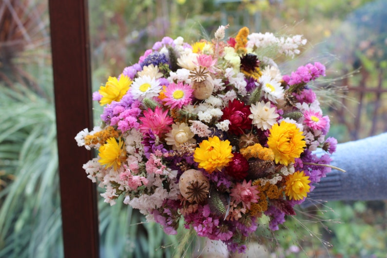 The pink and yellow bouquet being held in a hand. The details of the flowers shape are more obvious in this photo.