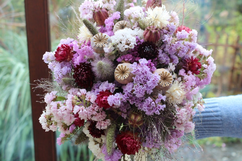 The purple bouquet being held in a hand. The details of the flowers shape are more obvious in this photo.