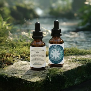 Puede incluir: Dos botellas de vidrio ámbar con cuentagotas negros, etiquetadas con texto que incluye "COUGH, COLD, IMMUNITY BLEND". Una etiqueta presenta un diseño floral azul y blanco. Las botellas están sobre una superficie musgosa cerca de un arroyo.