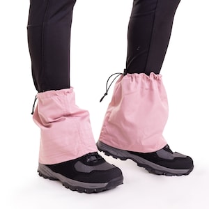 May include: A pair of pink gaiters with drawstrings, worn over black pants and black hiking boots.