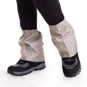 May include: A pair of black hiking boots with beige gaiters. The gaiters have a textured pattern and are worn over the ankles.