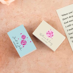 May include: Two rectangular cards featuring disco ball designs. One is pale blue, inscribed with "Jack & John" and "10/03/2025". The other is cream-coloured, bearing "William & Lucy" and "Jul. 25, 2026". Ideal for wedding or party favours.