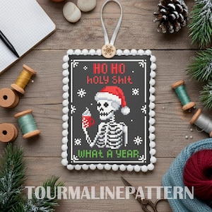 May include: A black and white cross-stitch Christmas ornament with a skeleton wearing a Santa hat and holding a mug. The text reads "HO HO HOLY SHIT WHAT A YEAR." The ornament is trimmed with white pom-poms.