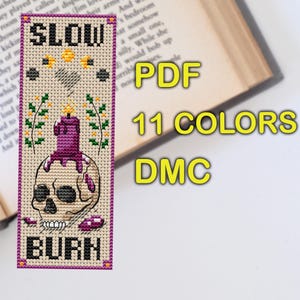 Cross stitch bookmark pattern on beige Aida with purple border: skull with a melting purple candle on top, wax drips, small flames, sprigs of flowers, stars, crescent moons, stitched heart, and text “SLOW BURN.” TourmalinePattern on Etsy.