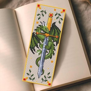 以下が含まれることがあります： 緑色のドラゴンと剣のデザインが施されたクロスステッチのブックマーク。 ドラゴンは、金の柄と銀の刃を持つ剣に巻き付いています。 ブックマークはクリーム色の背景、黄色のボーダー、装飾的な花の要素を備えています。 デザインは本の上にあります。