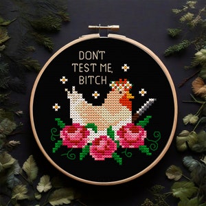 Puede incluir: Bordado de punto de cruz en un aro de madera con una gallina con un cuchillo, una corona de flores y flores rosas. El texto dice "DON'T TEST ME, BITCH" en letras blancas sobre un fondo negro.
