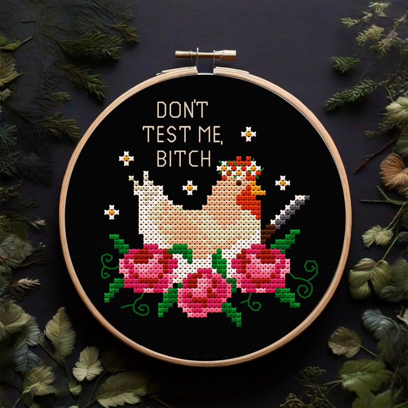 Puede incluir: Bordado de punto de cruz en un aro de madera con una gallina con un cuchillo, una corona de flores y flores rosas. El texto dice "DON'T TEST ME, BITCH" en letras blancas sobre un fondo negro.