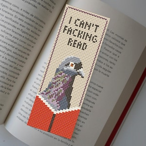 May include: A beige bookmark with a cross-stitch design of a gray pigeon reading a book. The bookmark has the text "I Can't Facking Read" on it.