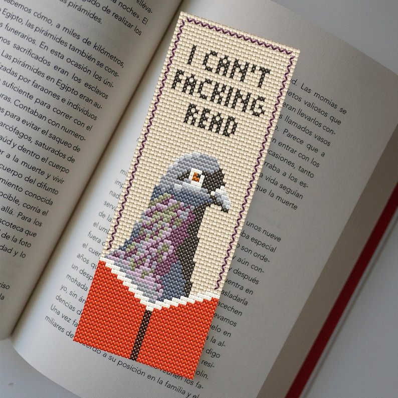 Puede incluir: Un marcap&aacute;ginas beige con un dise&ntilde;o de punto de cruz de una paloma gris leyendo un libro. El marcap&aacute;ginas tiene el texto "I Can't Facking Read".