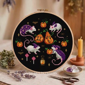 A cross-stitch design featuring white mice with purple capes interacting with pumpkins and other Halloween elements. The background is black, emphasizing the bright colors of the mice and pumpkins.