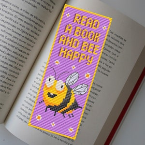 May include: A purple bookmark with a yellow and black cartoon bee. The bookmark has white flowers and the text "Read a Book and Bee Happy".
